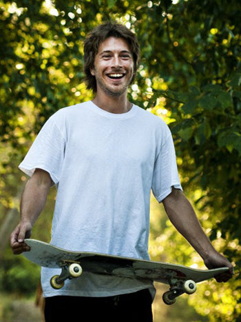 young man wearing white t-shirt smiling and holding skateboard like a serving tray
