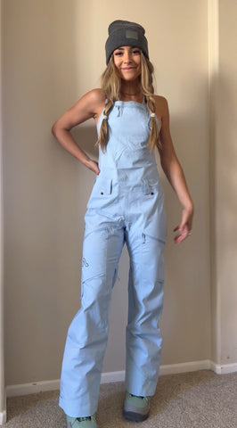 Girl standing in a blue Flylow bib in color Alpine