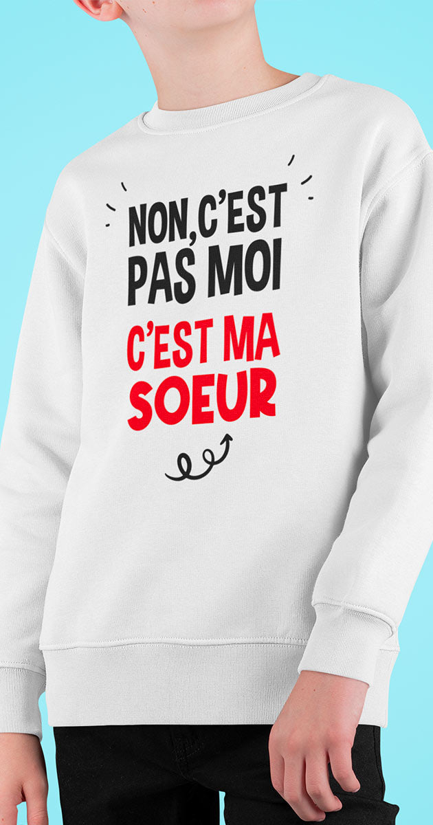 Garçon riant aux éclats tout en pointant son sweat où il est écrit "C'est pas moi, c'est ma sœur"