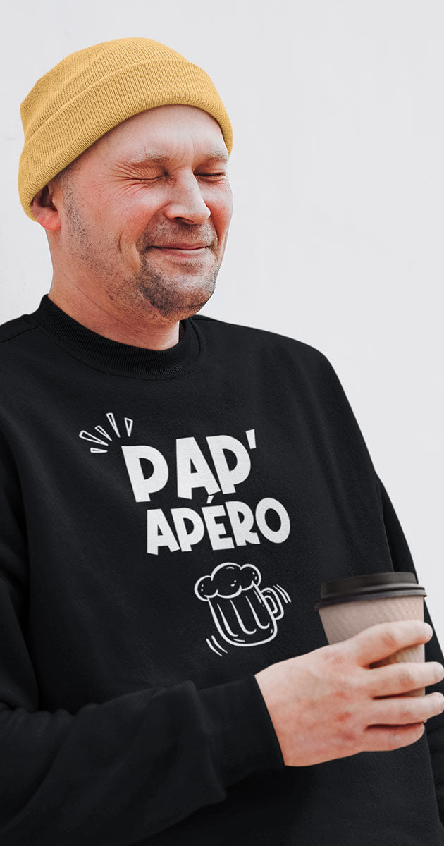 Papa souriant avec son verre en plein air, son pull "Pap'Apéro" reflétant son esprit festif