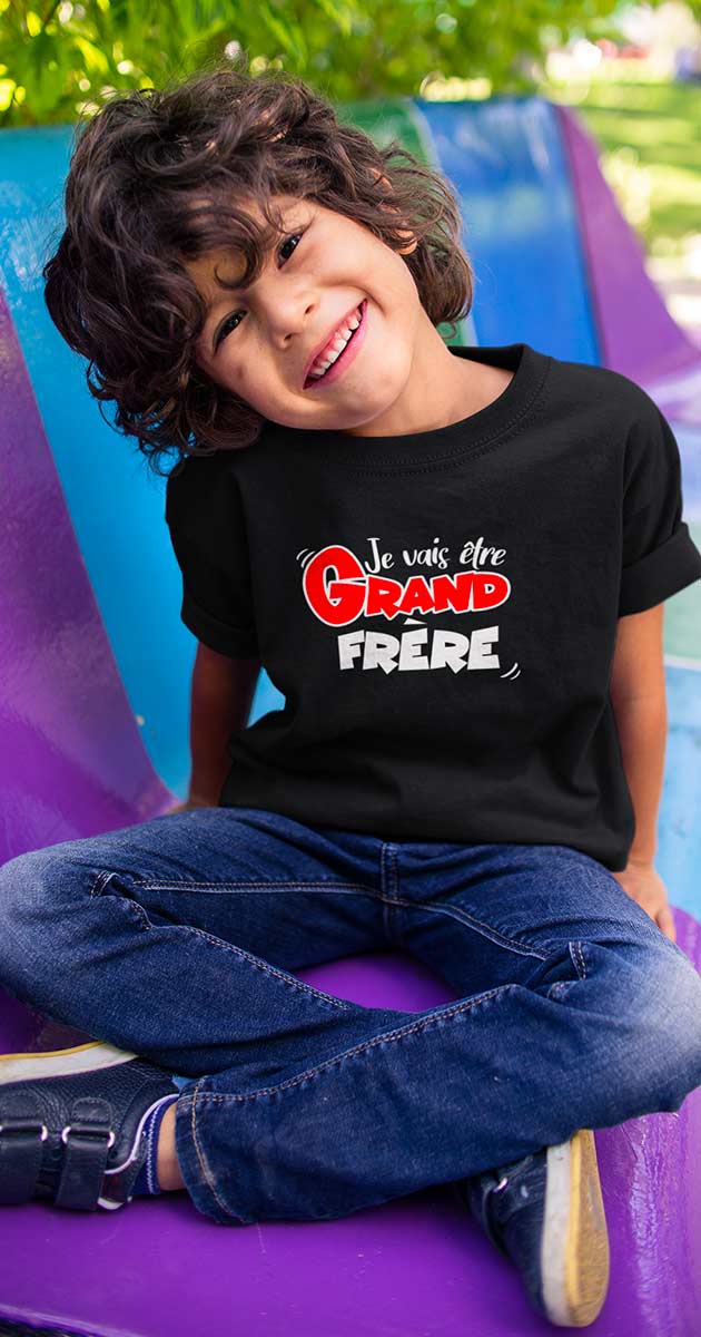 . Enfant souriant, portant le t-shirt "Je vais être grand frère", montrant fièrement le texte.