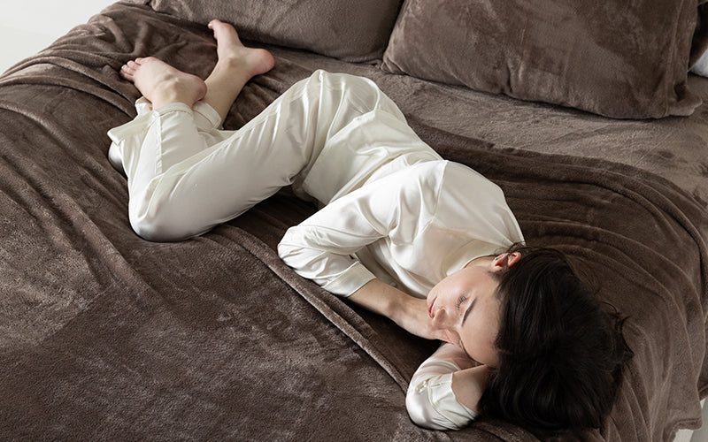 Woman in silk pajamas laying on a bed with taupe Velvetloft sheets