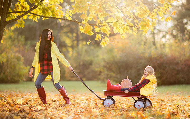 Woman pulling child in red wagon during autumn