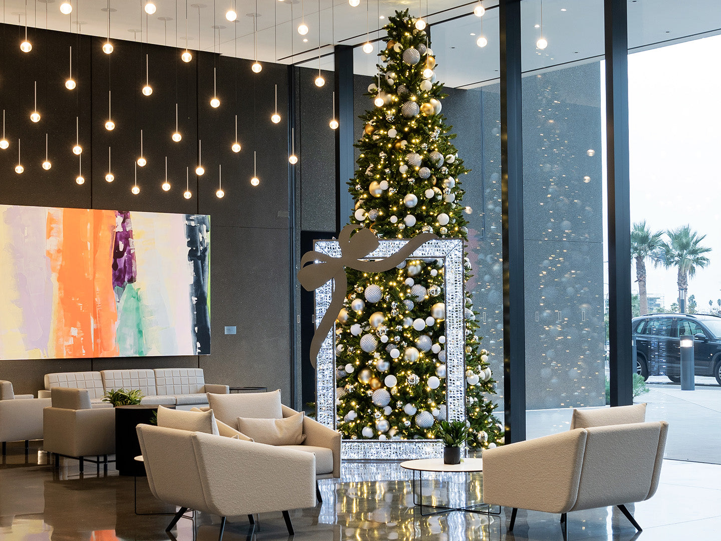 A towering Christmas tree, decorated in silver and gold ornaments, sparkles in front of an illuminated frame.