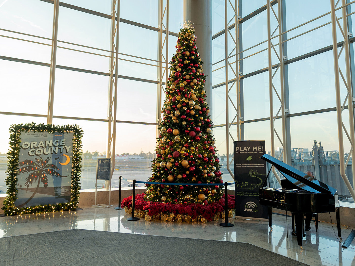 A Christmas tree adorned with vibrant poinsettias stands amidst the hustle and bustle of an airport terminal.