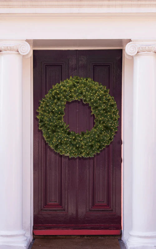 A lush wreath lit up with warm LED mini lights is adorned to a front door.