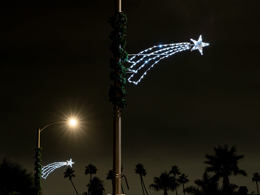 A decorative white shooting star mounted on a lamp post, creating an illusion of a shooting star in an urban setting at night.