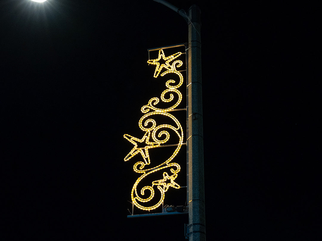 A light pole decorated with festive Christmas lights, including a swirl pattern and star shapes, at night.