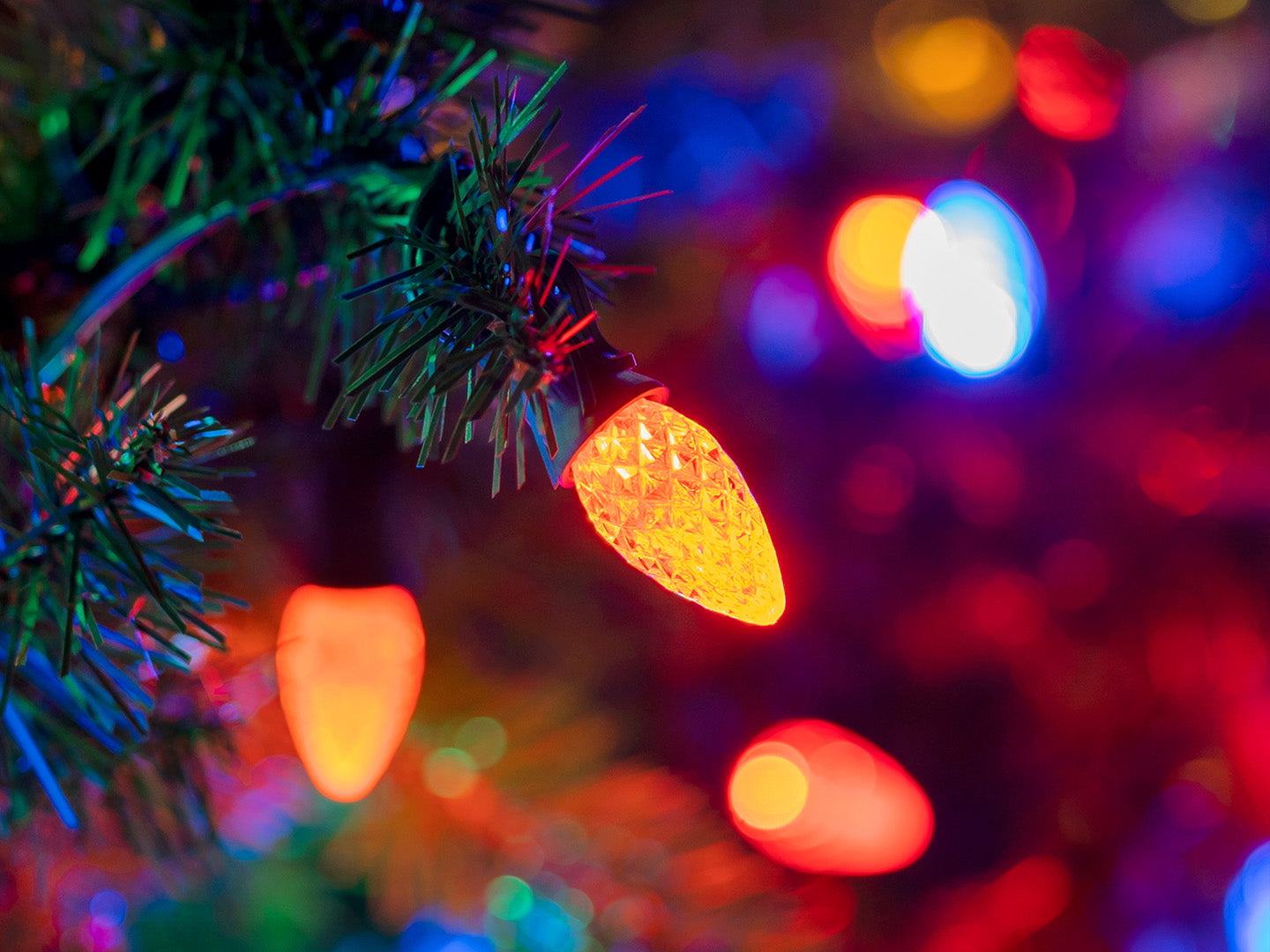 A close-up picture of an orange faceted C7 light bulb in a Christmas tree surrounded by blurred multicolor lights in the background.