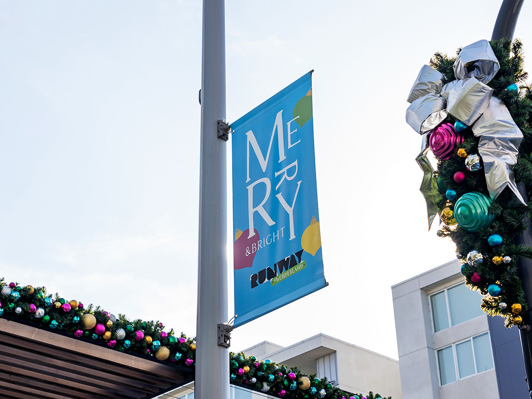A holiday display featuring a blue banner with white text that says "MERRY" & "BRIGHT" next to a festive Christmas spray. The spray has a silver bow and various ornaments.