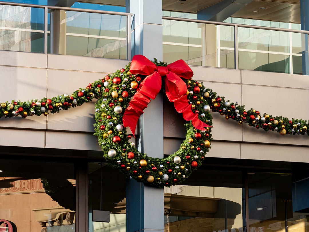 A traditional Christmas decoration: a wreath with a red ribbon and garland swag, displayed on the exterior of a building.