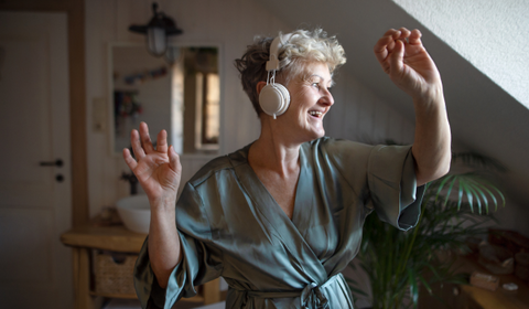 Happy Older Woman Dancing In Dressing Gown With Headphones On