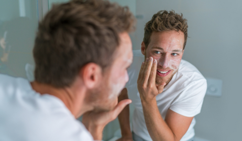 Man Putting On Face Scrub In Front Of Mirror