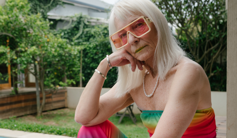 older woman dressed in rainbow outfit and sunglasses sitting in garden