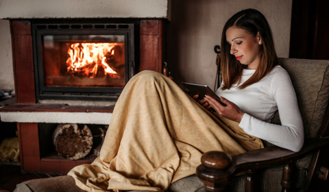 Women wrapped in blanket reading by the fire for Autumn Wellness