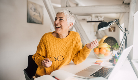 Happy Older Woman Laughing At Computer Desk With Open Laptop