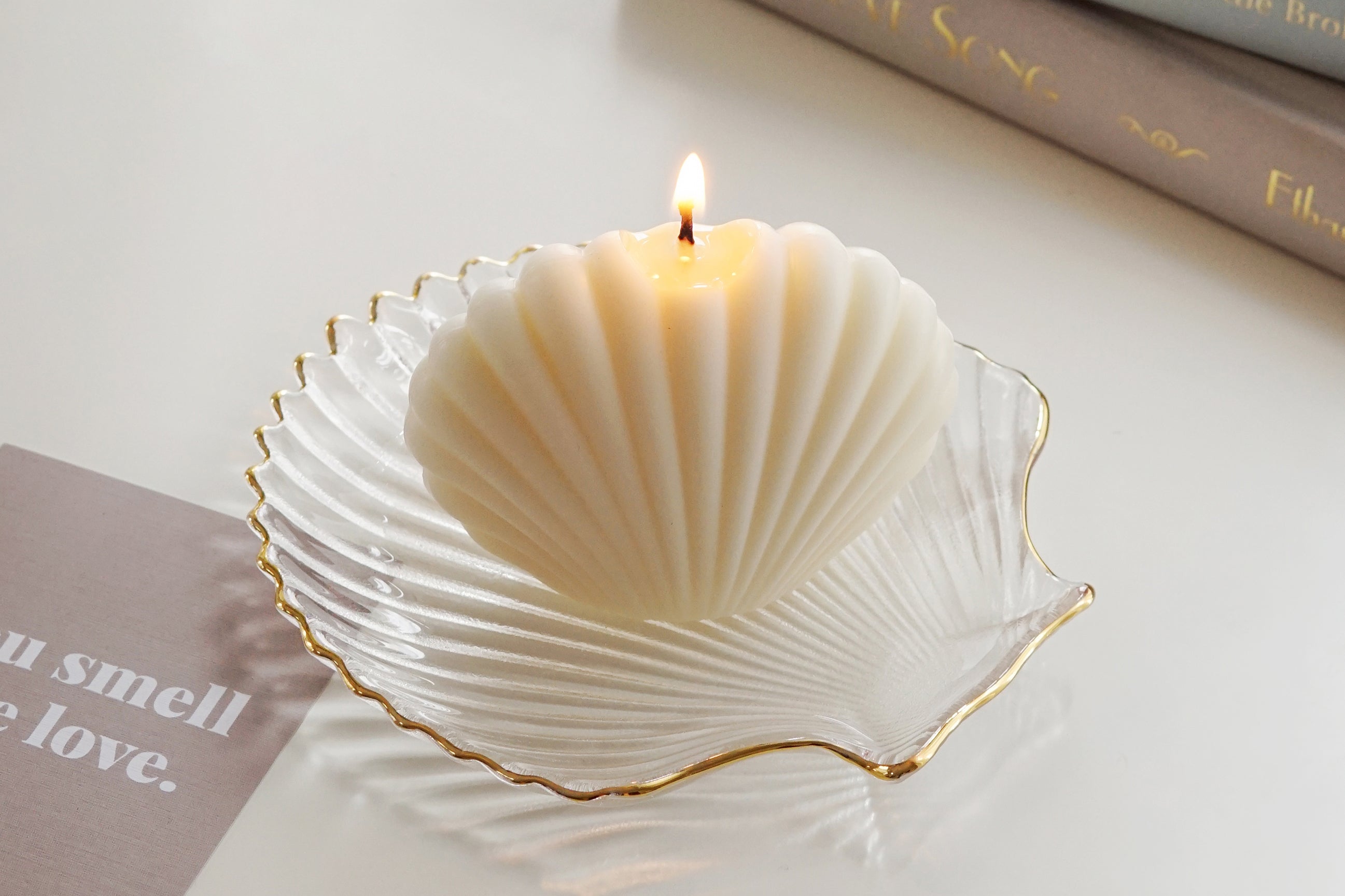 a lit seashell soy pillar candle on clear shell tray