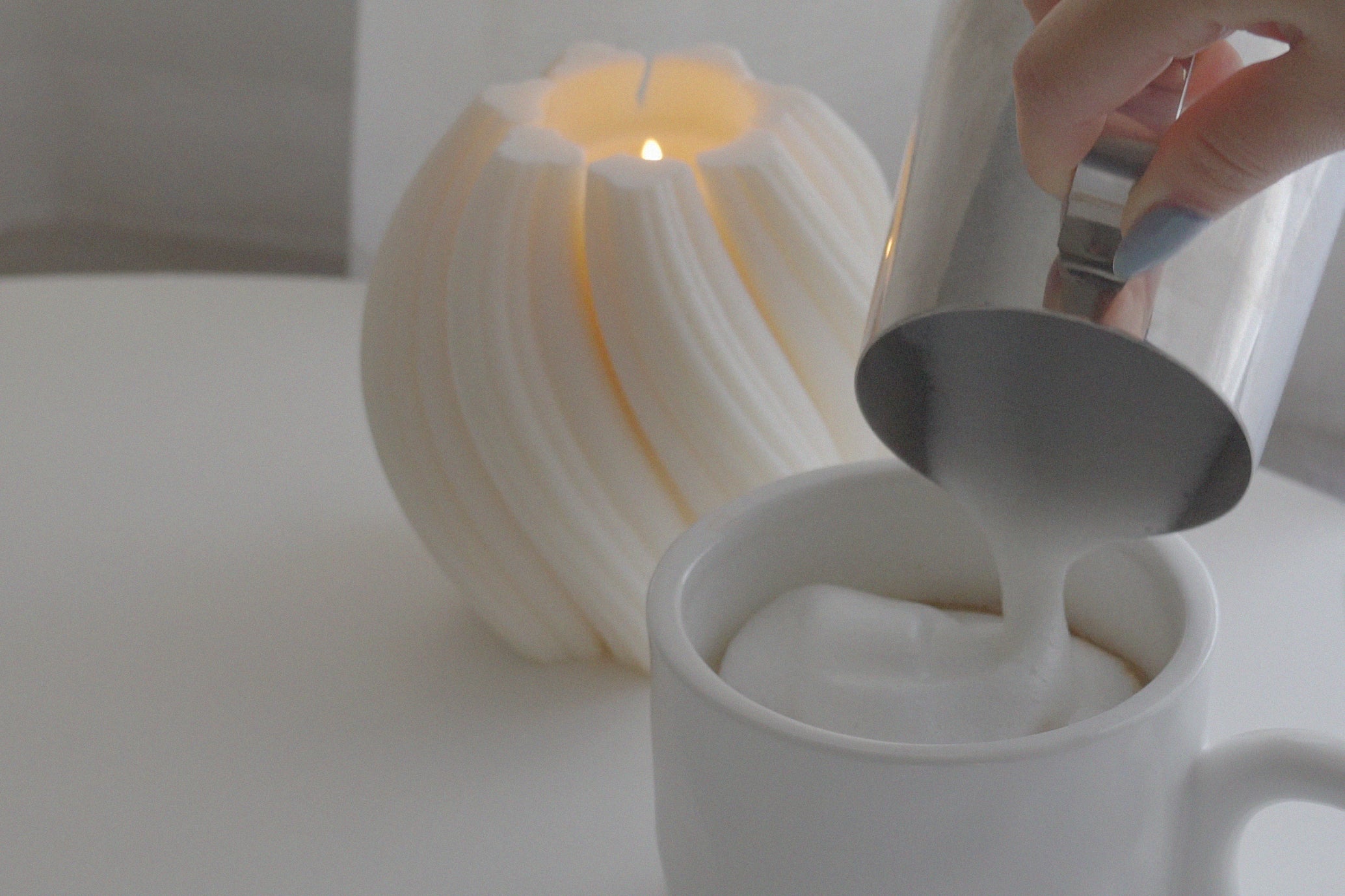 pouring cream on top of a cup of latte in a mug with a lit swirl objet candle