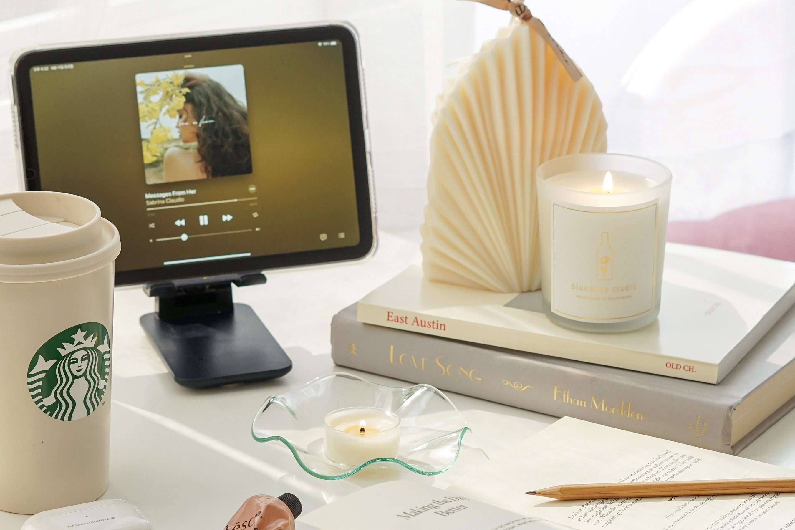 Ipad, vaso de Starbucks, libros, lápiz y velas sobre la mesa.