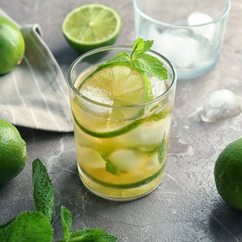 Mint Julep mocktail garnished with lime slices and fresh mint in a glass on a textured gray surface