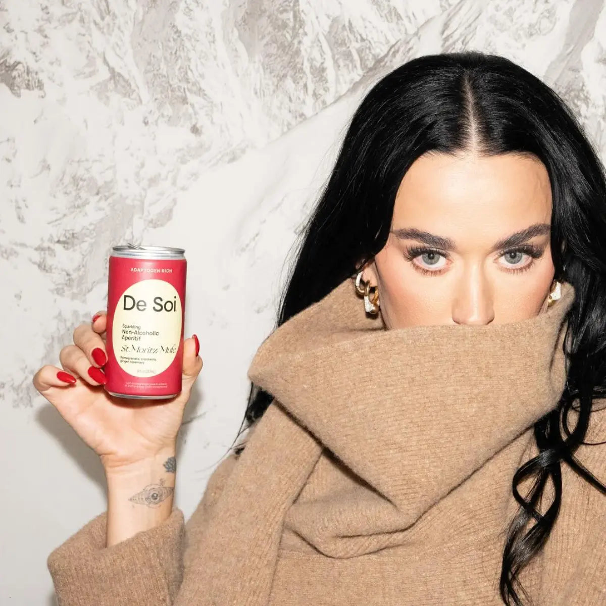 Mocktail in a can held up by a woman in a tan sweater against a snowy mountain backdrop