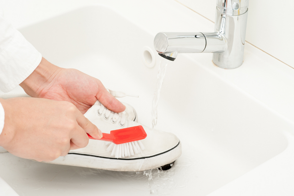 Person cleaning white canvas sneakers in sink