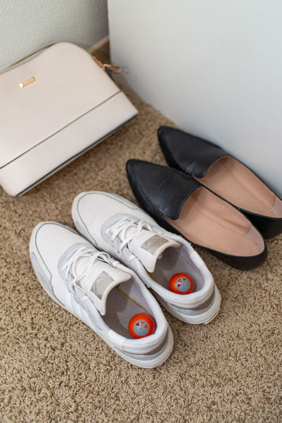 sneaker deodorizer balls inside white tennis shoes in closet with flats and purse