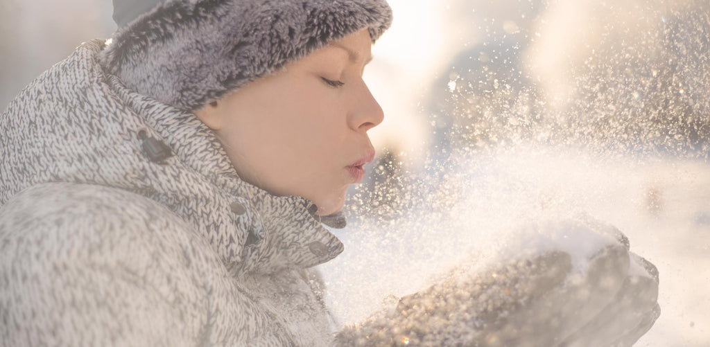 Woman playing in the snow, blowing snow from hands