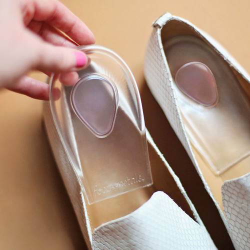 Person putting gel heel cup cushion into white alligator skin flats