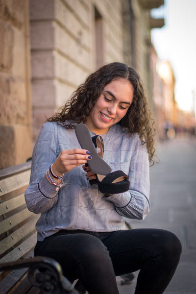 woman seated on a bench placing a ¾ insole cushion into a black platform heel