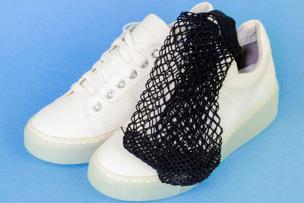 Pair of white sneakers with black fishnet socks