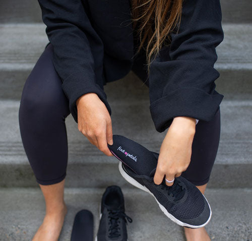 Woman sitting on steps placing black shoe insole into black tennis shoes