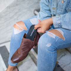 Woman placing Foot Petals orthotic insole in brown ankle boot