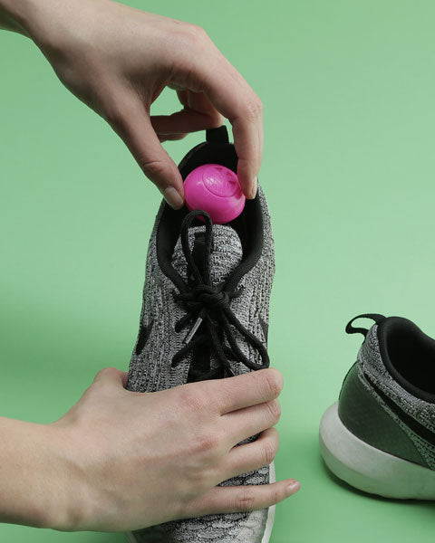 woman placing pink shoe deodorizer ball in gray running shoe