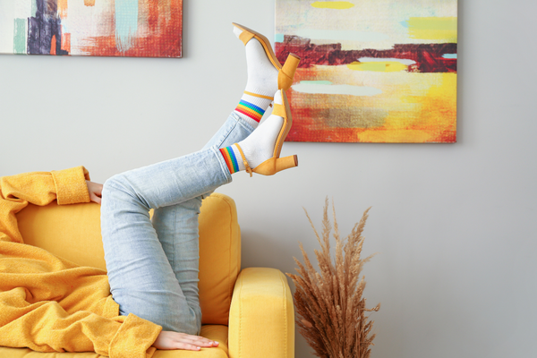 Woman on couch wearing white rainbow socks with yellow heels