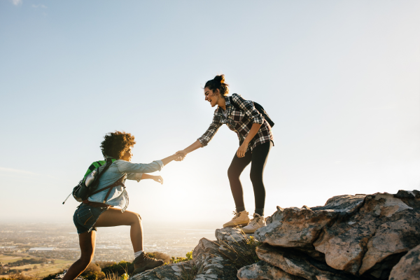 One woman helping another woman up a rocky hill while hiking