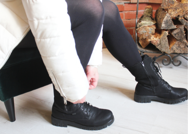 Person in coat sitting down and tying black combat boots