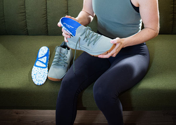 Woman placing PowerStep bridge comfort insole inside tennis shoe