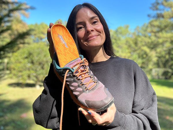 Woman standing outside holding tennis shoe with PowerStep PULSE orthotic insoles inside.