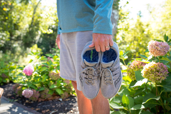 Man carrying gray tennis shoes with blue orthotic insoles inside