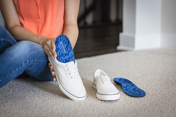 Woman holding white shoe with blue PowerStep Original orthotic insole
