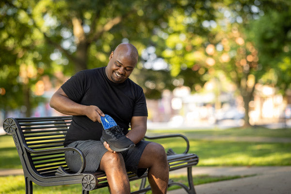 Man sitting on park bench and placing blue insole into black shoe