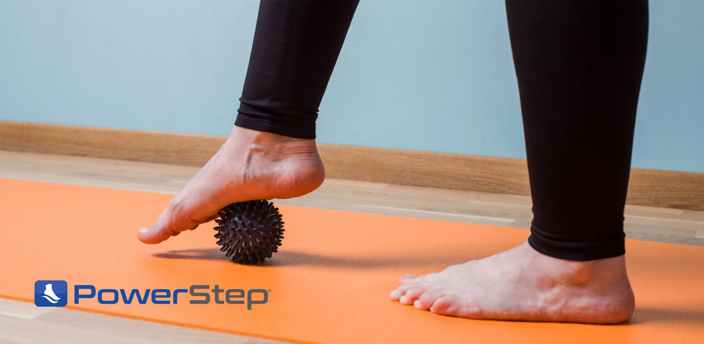 Person rolling black massage ball under foot