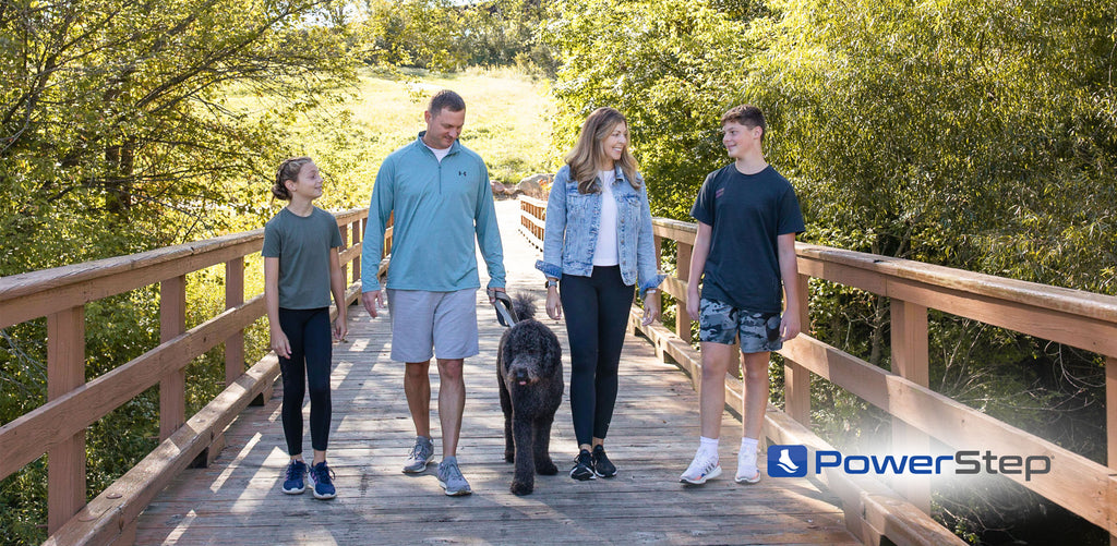 family of four walking a black dog across a bridge