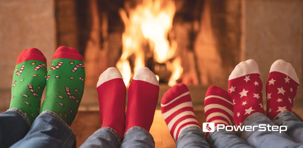 Four people wearing holiday socks warming feet by fireplace