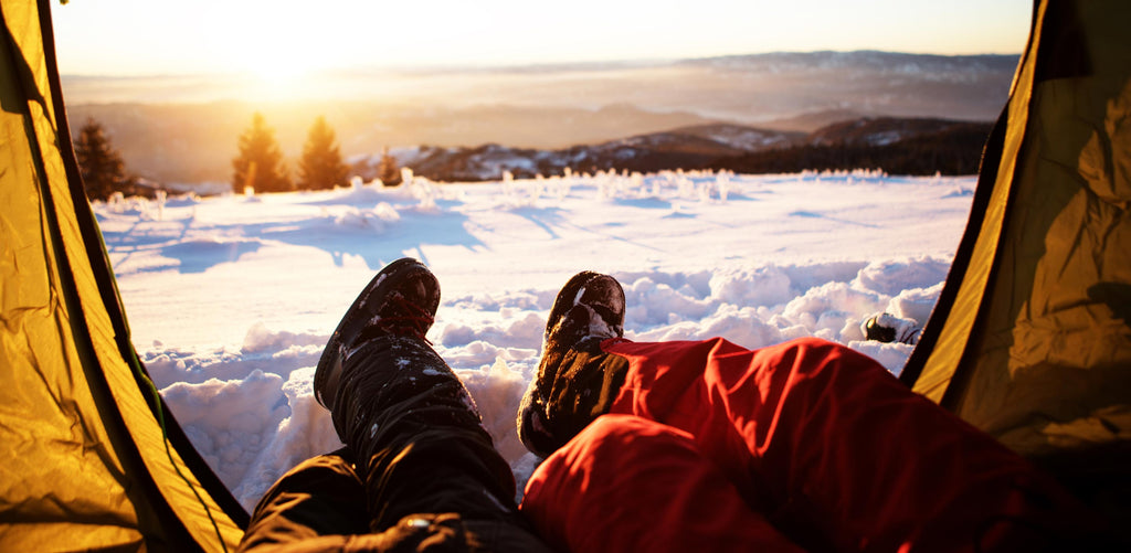 Couple camping in the winter time, enjoying the view of snow from their tent