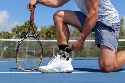 Tennis player kneeling to adjust ankle brace sock on the court