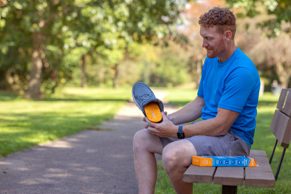 Man sitting on outdoor bench while placing orange running insole into gray shoe