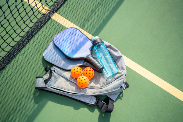 Pickleball rackets, balls, and water bottle with backpack on green court