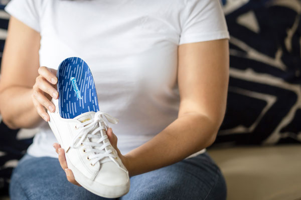 Woman placing blue shoe insole into white tennis shoe
